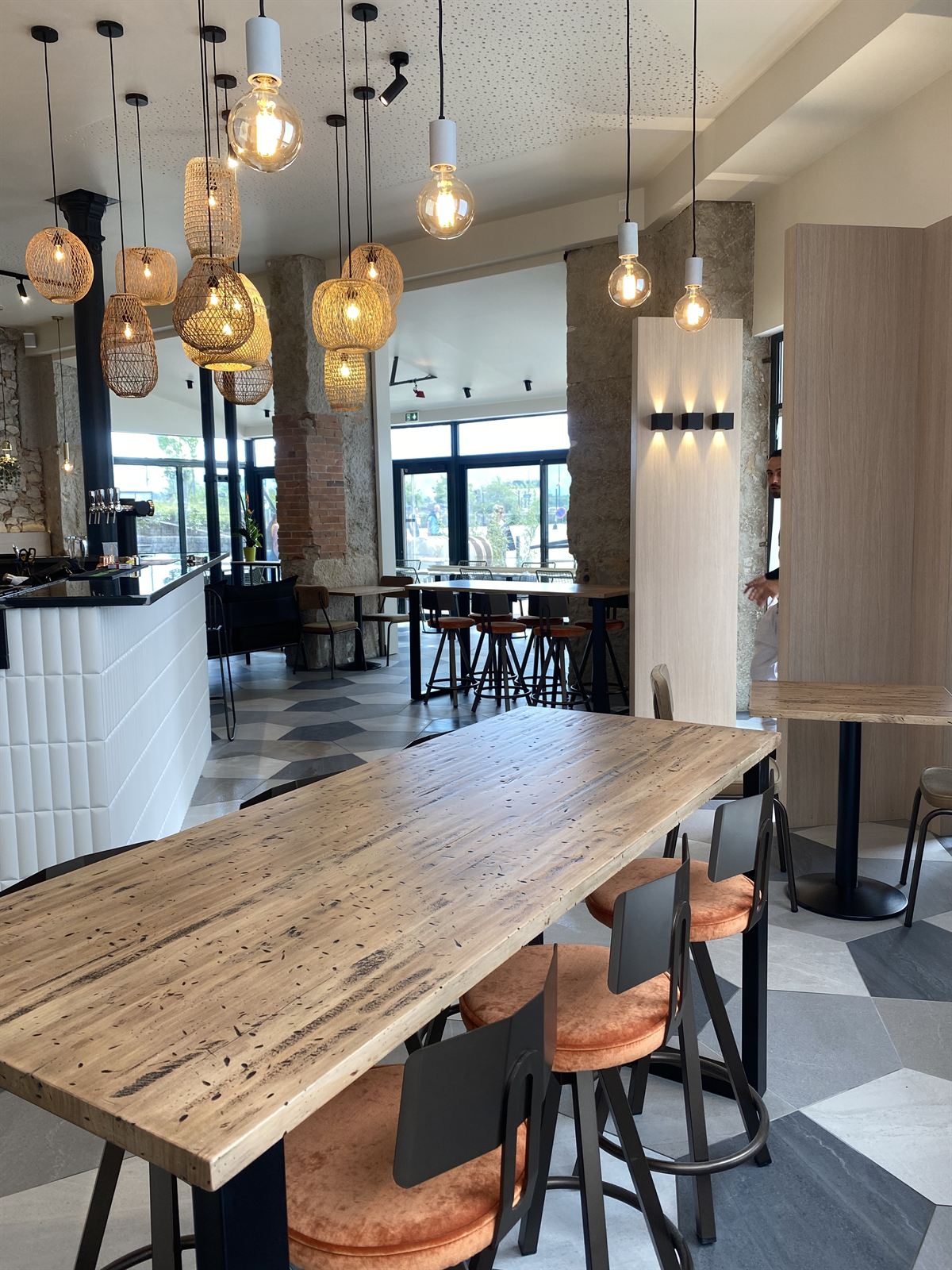 La salle de La Badiane : grande table en bois brut, suspensions en rotin et pierre apparente